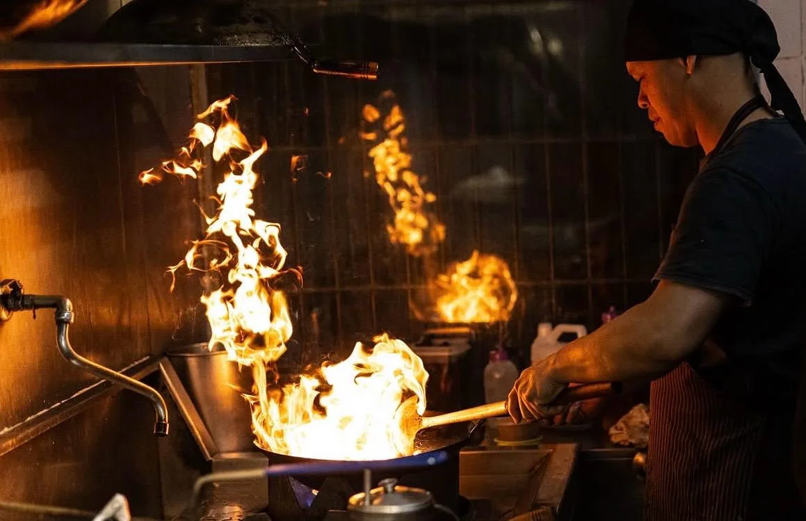 Cocinero salteando al wok entre llamas en la cocina de Sudestada